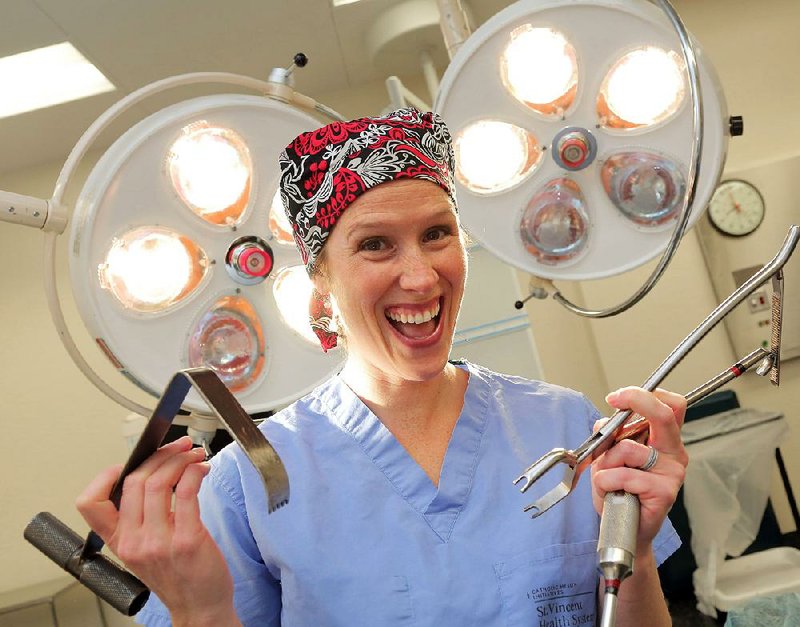 Inside an operating room at CHI St. Vincent Infirmary, Dr. Kate McCarthy holds up a large muscle retractor (left) and a compressor, orthopedic surgical tools. In a few weeks she’ll be extending and expanding young girls’ minds as a volunteer for the Perry Initiative. 