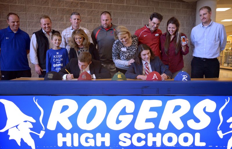 Sage White (left) and Harrison Heffley, surrounded by family and coaches, sign Friday during a ceremony at Rogers High. White signed to play baseball for Harding and Heffley for Arkansas.