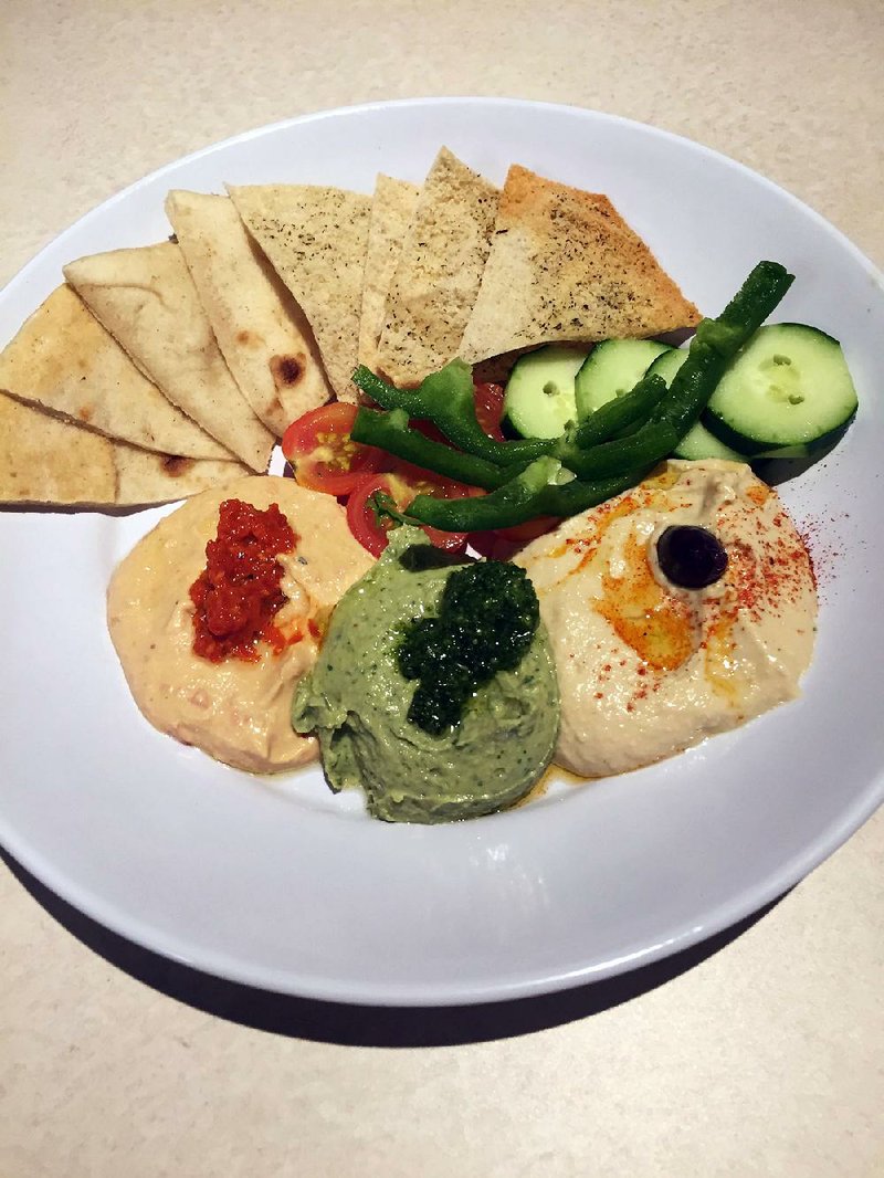 The Hummus Trio features basil pesto, red pepper and classic hummus with pita chips, tomatoes, green peppers and cucumbers at Zoes Kitchen. 