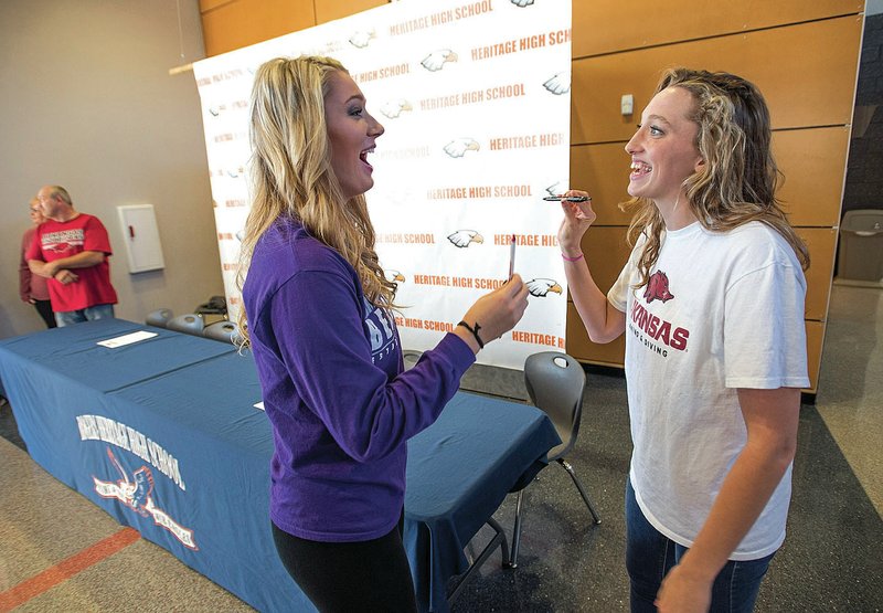 Rogers Heritage seniors Elleson Dunagin (left) and Carly Holland laugh Wednesday before joining their families and coaches in a letter of intent signing ceremony. Dunagin signed to play volleyball at Central Arkansas, while Holland signed with Arkansas for swimming.