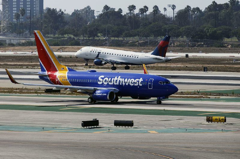 A Southwest Airlines Boeing 737-700 taxis to Terminal 1 as a Delta Air Lines Inc. Embraer SA 175 lands at Los Angeles International Airport in August. Commercial jets spent 23 minutes and 32 seconds, on average, taxiing between gates and runways during the fi rst nine months of the year, according to an Associated Press study.