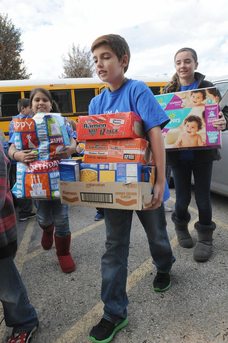 Ryan Gray (center), student at Elza Tucker Elementary in Lowell, carries food items with other fifth-graders Tuesday into Lowell First Baptist Church. Students in Candace Pierce’s fifth-grade class organized a food drive that saw more than 3,800 food items donated.