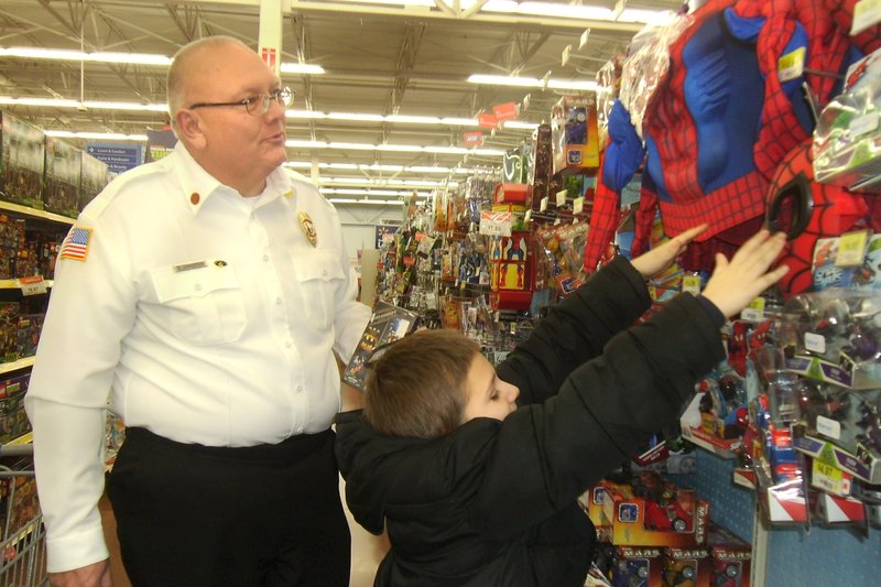 Submitted photo Pineville Fire Chief and Mayor Greg Sweeten help a youngster channel his inner superhero during last year&#8217;s &#8220;Shop With a Hero&#8221; event.