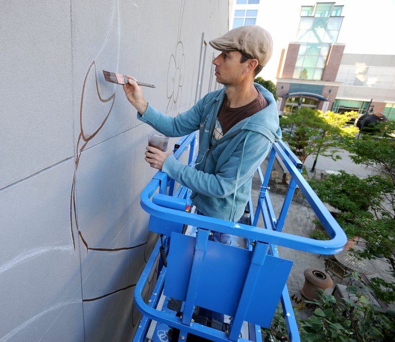 Jason Jones, a Fayetteville-based artist, paints Aug. 20 while working on a mural on the east wall in the plaza outside the Fayetteville Town Center.