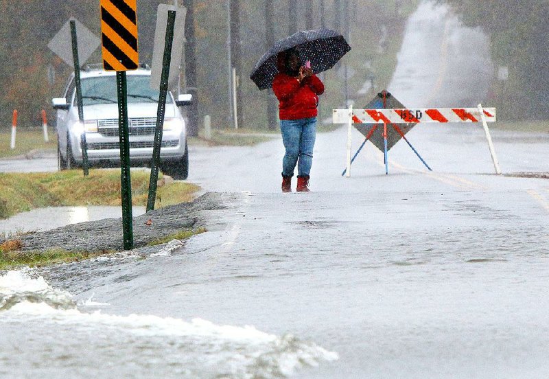A woman photographs water running Saturday over a closed section of Boone Road in Bryant. Water flooded a large portion of Bishop Park along Boone Road. 