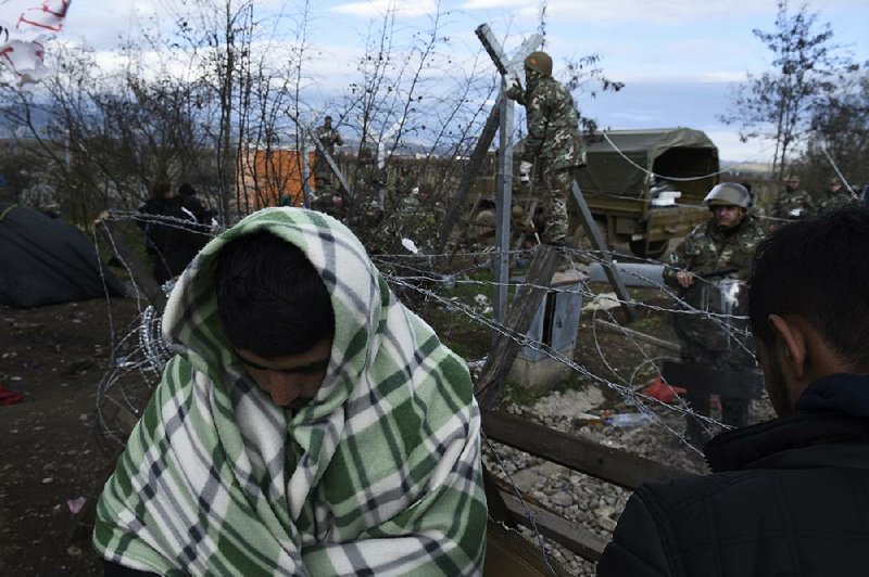 Migrants wait behind barricades Sunday as Macedonian soldiers build a fence at the Greek-Macedonian border near the northern Greek village of Idomeni. Many migrants in Greece arrive by sea from Turkey, which on Sunday agreed to help the European Union in preventing the travels of those who do not need international protection.