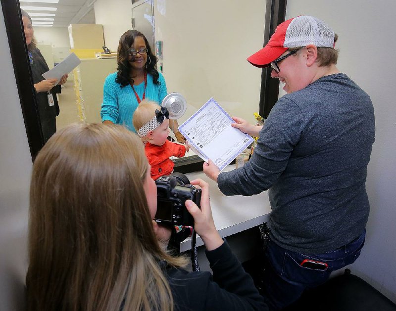 Marisa Pavan shows 6-month-old daughter Tucker Ruth Pavan her amended birth certificate after it was issued Wednesday at the Arkansas Vital Records office in Little Rock. Pavan and her wife, Terrah Pavan (left), had sued to have Marisa’s name added to the certificate. 