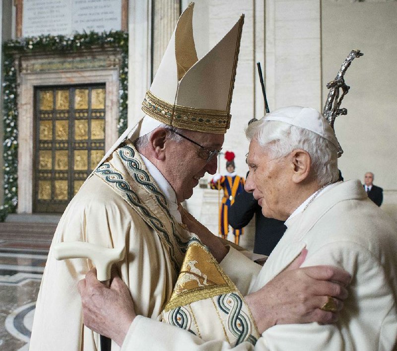 Pope Francis (left) embraces his predecessor, Emeritus Pope Benedict XVI, before opening the Holy Door (background) at St. Peter’s Basilica. The 88-year-old Benedict followed the pope through the door with the help of a cane and an assistant. 