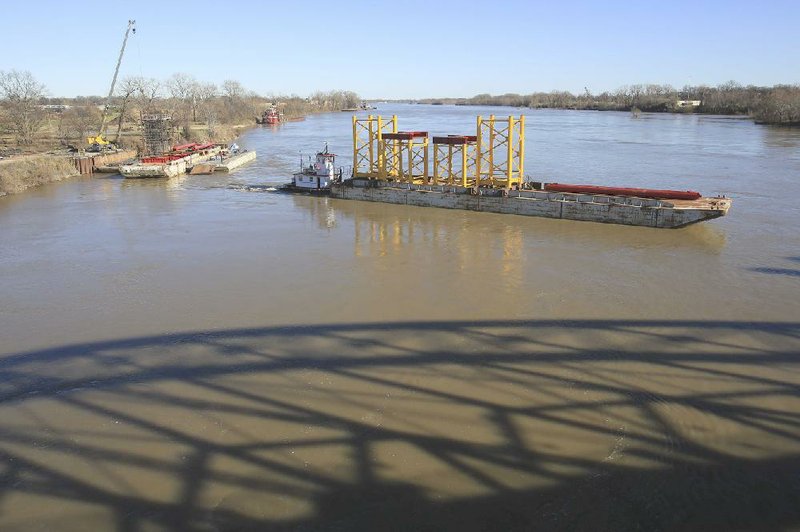 Large towers that will support construction of the new Broadway Bridge are moved into place on the Arkansas River by a barge Monday near the shadow of the Clinton Presidential Park Bridge.