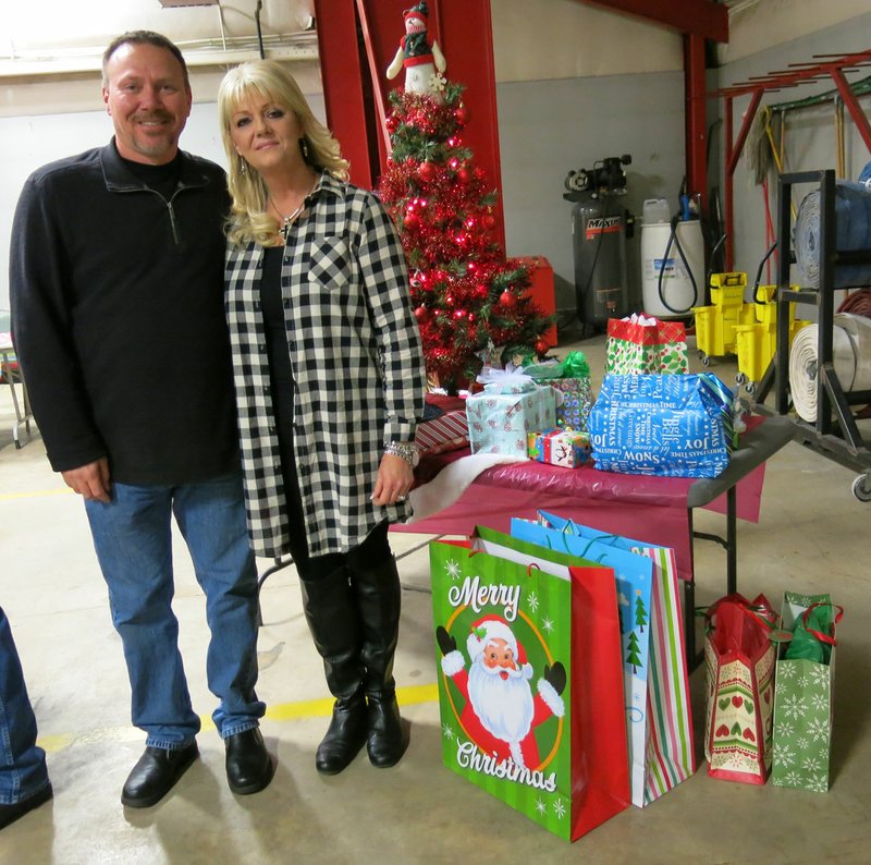 Photo by Susan Holland Rob Douthit, chief of the Gravette Fire Department, and his wife Karen posed in front of the department&#8217;s Christmas tree in the big truck bay at the fire station Saturday evening. Douthit revived the tradition of a holiday dinner to honor retirees and the fire trucks were moved outside to make room for the evening&#8217;s celebration. Guests who brought gifts to put under the tree participated in a gift exchange after the dinner.