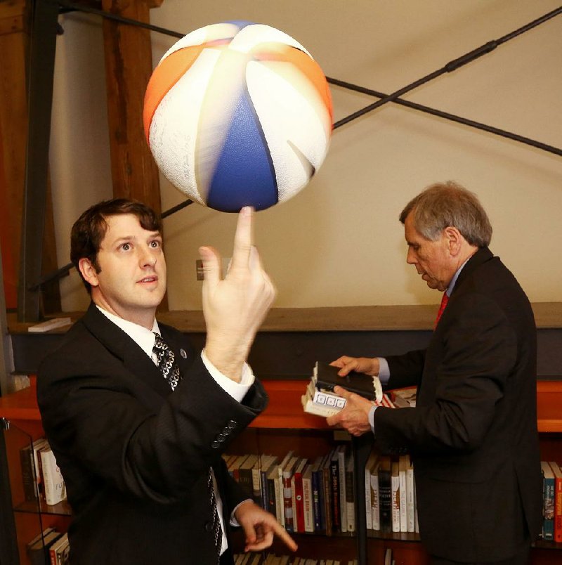 Nikolai DiPippa, director of public programs at the Clinton School of Public Service, spins a basketball signed by Bill Bradley, basketball Hall of Famer and former U.S. senator, D-N.J. Dean Skip Rutherford concentrates on the school’s collection of signed books.