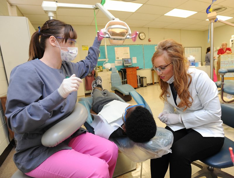 Dr. Jenna Waselues (right) checks on a patient Dec. 11 with the help of student Megan Jackson at the Agee-Lierly Life Preparation Services School of Innovation in Fayetteville. Waselues is a dentist and graduate of Fayetteville High School and the University of Arkansas who has returned to the area and volunteers her time to assist in mentoring students in the dental assistant program. For more photos, go to www.nwadg.com/photos.