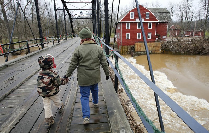 Shayna Wolf walks across the War Eagle Bridge on Tuesday with son Reuben, 5, after the War Eagle Creek receded and allowed access to the War Eagle Mill on the east side of the creek. Water from the creek rose out banks and into the mill.