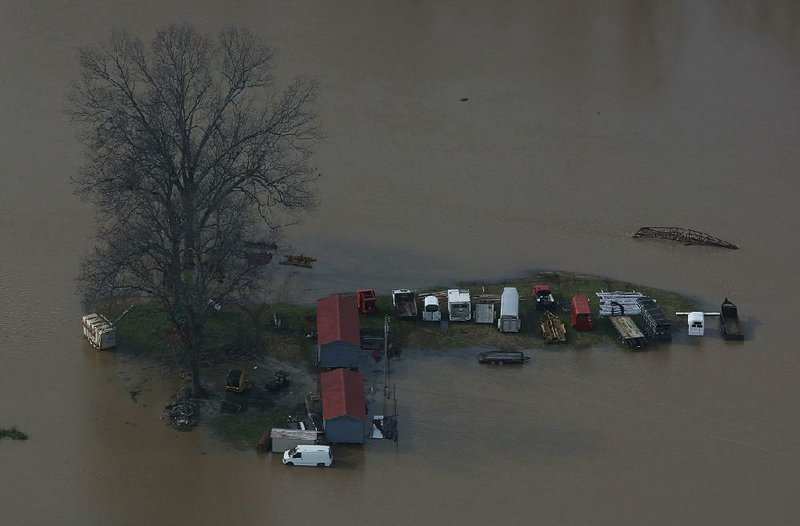 Farm equipment is stranded Thursday as floodwaters from the Arkansas River rise near Bigelow. Flooding in the area near Toad Suck levee isn’t uncommon, and landowners there expressed frustration Thursday that repairs haven’t been made to the levee to reduce flooding in the area. 