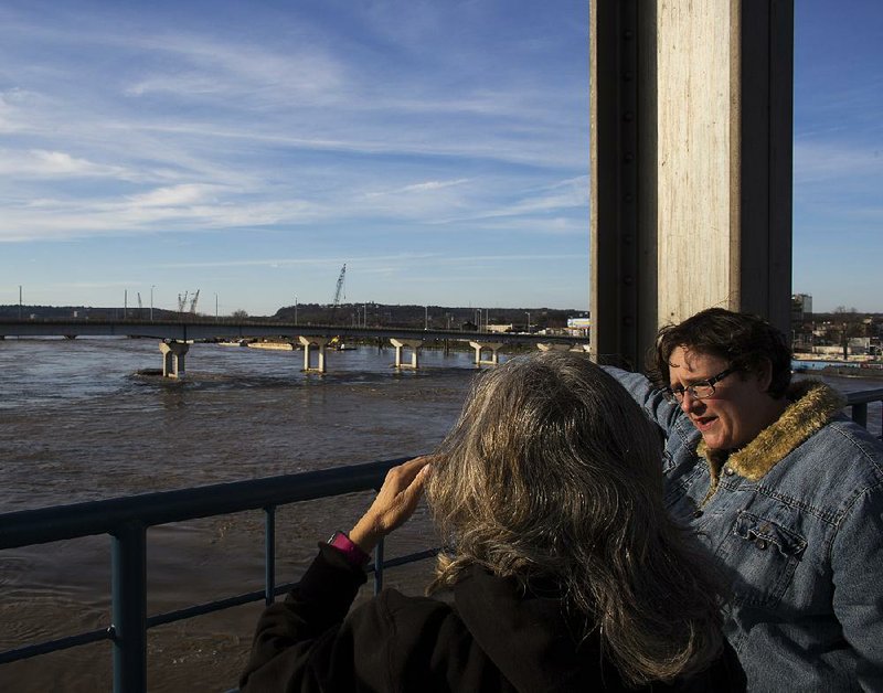 Suzanne Spearman (right) describes the usual pattern of the Arkansas River to visitor Diana Soto of New Mexico on Saturday as they walk along the Junction Bridge in Little Rock. The river was at 24.9 feet Saturday in Little Rock.