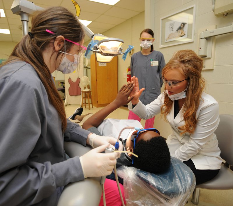 Dr. Jenna Waselues (right) gets a high five from a patient Dec. 11 as students Rachel Johnson (from left) and Lillian Israel assist at the Agee-Lierly Life Preparation Services School of Innovation in Fayetteville. Waselues is a dentist and graduate of Fayetteville High School and the University of Arkansas who has returned to the area and volunteers her time to assist in mentoring students in the dental assistant program. For more photos, go to www.nwadg.com/photos.