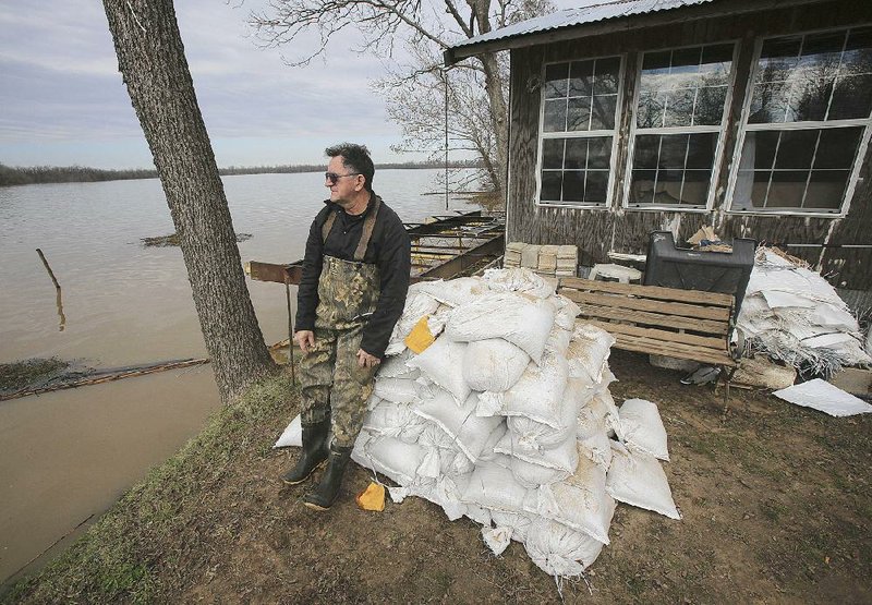 David Adamson leans on a pile of unused sandbags Sunday afternoon at his house on Marion Drive in Wright. Adamson said the water level around his house is starting to drop.