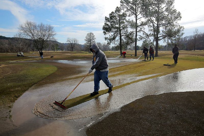 Rebsamen Park Golf Course workers clean Arkansas River silt from the No. 3 green in Little Rock on Wednesday morning. The job required one team with water hoses and another of equal number to squeegee away the mud. “It’s like washing peanut butter out of Velcro,” one worker said.