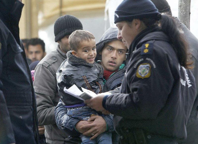 A Greek police officer checks the identification documents of migrants before allowing them to cross the border Monday from Greece into Gevgelija, Macedonia. Dozens of Hungary’s officers along with police officers from Serbia and Croatia have been sent to Macedonia to help manage the flow of migrants.