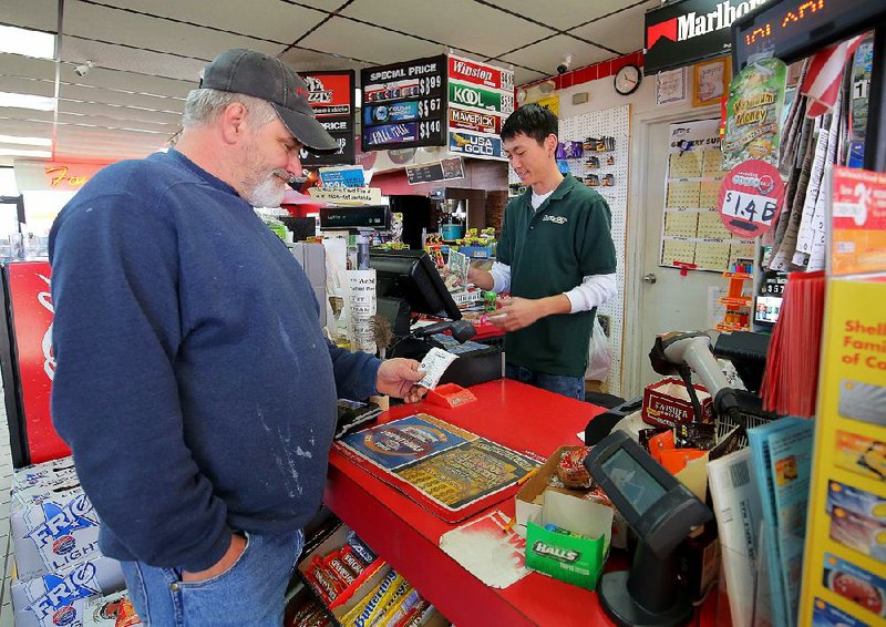 John Webb of Bryant looks at a Powerball ticket he bought from Y&E Superstop manager Michael Park on Tuesday morning at the store in Bryant. 