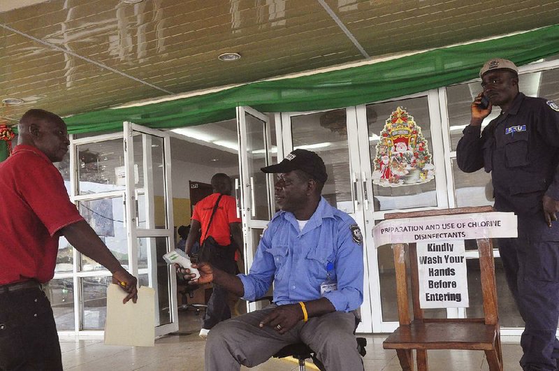 A health worker takes a man’s temperature before allowing him to enter a government building Thursday in Monrovia, Liberia, where a sign asks visitors to wash their hands.