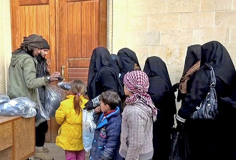 Members of the Islamic State group (left) distribute niqabs, enveloping black robes and veils that leave only the eyes visible, to Iraqi women in Mosul, northern Iraq, in this photo released on Jan. 31, 2014.