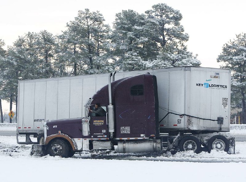 A trucker clears snow from the cab while waiting for a tow after his rig jackknifed Friday on the westbound 65th Street on-ramp to Interstate 30 in south Little Rock. 