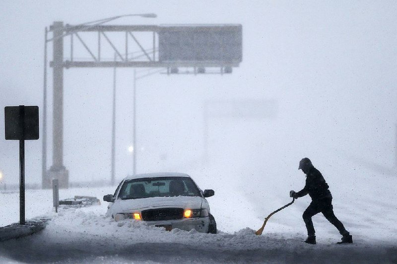 A motorist shovels snow to try to free a car stuck on the New Jersey Turnpike in Port Reading during a snowstorm that paralyzed much of the East Coast on Saturday.