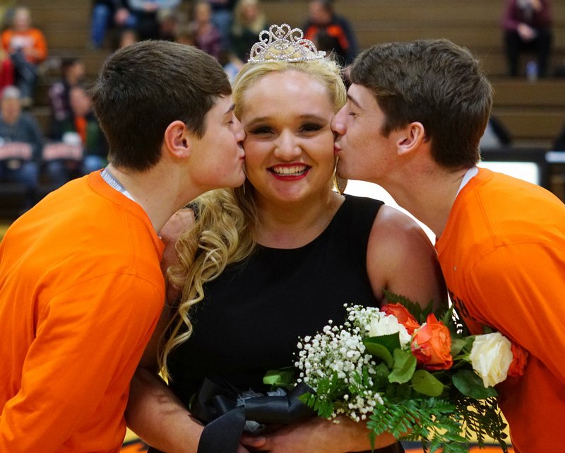 Photo by Randy Moll Jaye Chalk, Gravette senior, received a kiss from her escorts, Thomas Reynolds and Tanner Pike, after she was crowned basketball homecoming queen at Gravette High School on Friday night.