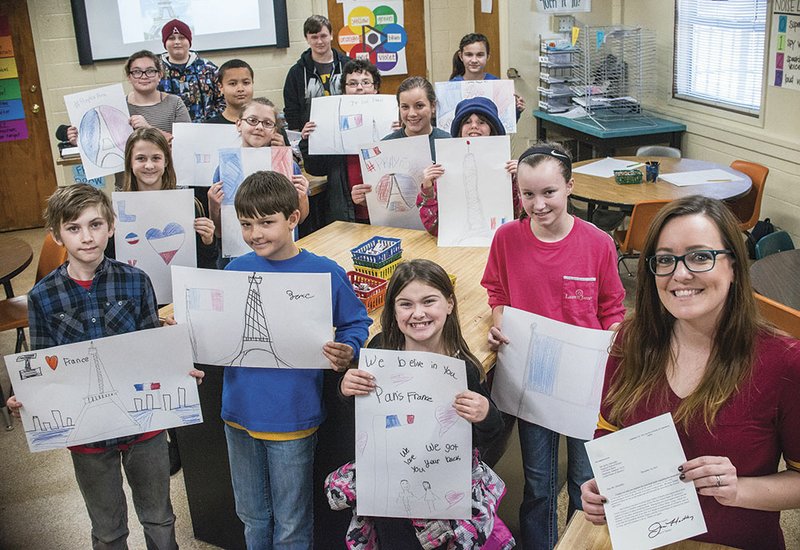 Pangburn Middle School art teacher Kelly Abernathy, far right, holds the letter sent from Jane D. Hartley, the U.S. ambassador to France, after students from the school sent artwork in support of the French after the Paris attacks. Students Brittan Piety, front row, from left, Zane Waters, Kira Atkins and Emma Reaper; second row, Elizabeth Newman, Becca Wenger, Blakely DePriest and Kaelyn Freese; third row, Cassie Reed, Brock Mangthag and Justin Hendrix; and top row, Gage Baty, Gavin Smith and Courtney Vess all hold up their artwork, which was just some of the pieces the school sent to Paris.