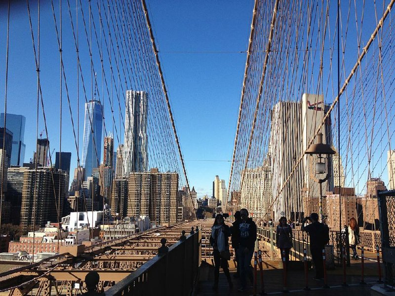 Visitors to the Brooklyn Bridge take photos with the Manhattan side in the background. The upper span of the bridge is open to pedestrians and bicyclists 24 hours a day, 365 days a year.