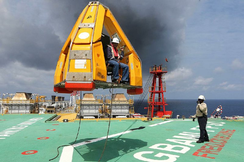 An oil worker sits in a frog basket as he is lowered onto the deck of the fl oating production vessel Agbami, operated by Chevron Corp., in an offshore oil field in Nigeria in November.