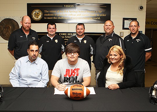 The Sentinel-Record/Richard Rasmussen RED ALERT: Hot Springs defensive lineman Dante Ibarra, sitting center, signs his national letter of intent to play for Henderson State. Joining Ibarra at the ceremony Wednesday were seated, from left, father Brian Galbreth and mother Christina Ibarra; standing, coaches Doug Shott, Cory Sturdivant, Chris Vereen, Reid Kauffman and Matt Gonzales.