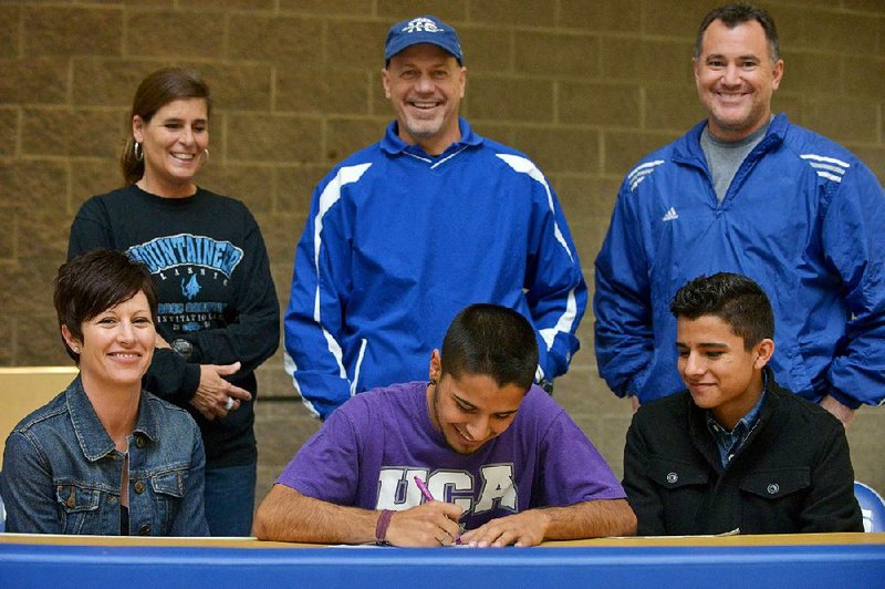 Austin Salazar signs a national letter of intent to run track and cross country at the University of Central Arkansas with mother Emily Salazar and brother Christian Salazar, front row, and coaches Becky Efurd, back row from left, Carlton Efurd and Jim Yurwitz, during a ceremony in the commons at Rogers High on Friday Dec. 5, 2014. 