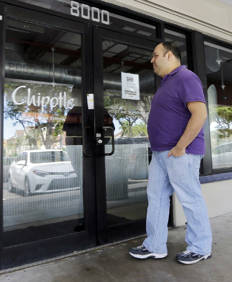 Jose Espinosa looks into a closed Chipotle restaurant on his lunch break on Monday in Miami Lakes, Fla. Chipotle restaurants across the United States opened later than usual Monday as workers gathered to discuss the chain’s recent food safety scares.