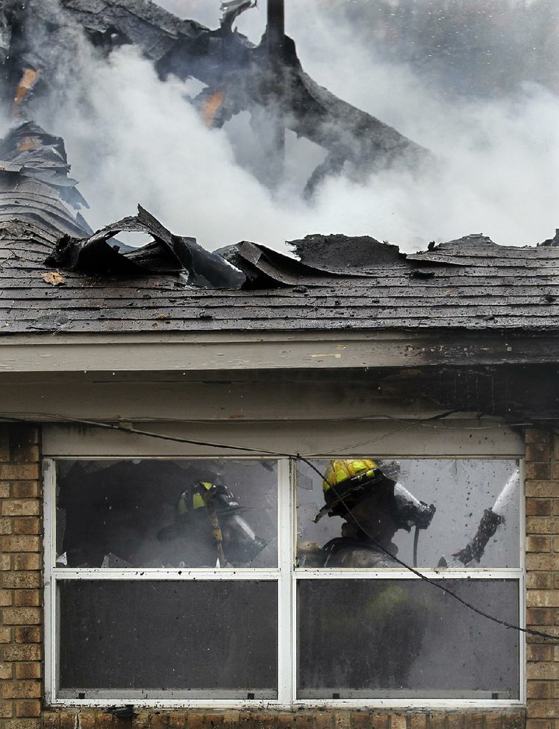 Little Rock firefighters douse a fire at a house on Walpole Drive on Monday morning. The cause of the fire was unclear. Firefi ghters throughout Arkansas also fought wind-driven brush fires.