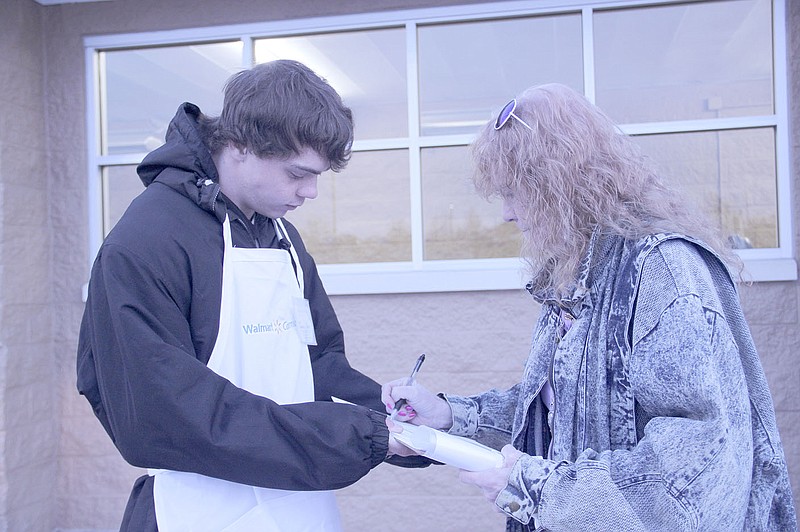 LYNN KUTTER ENTERPRISE-LEADER Kelly Lopez, of Farmington, right, signs a petition Friday evening outside Walmart Neighborhood Market asking that the question of whether to allow alcohol sales in the city limits be placed on the Nov. 8 election ballot. Jason Boje was one of three people canvassing for signatures outside the front of the store. Growth for Farmington has hired Blueprint Action to run the petition drive. The in-field director is Tim Fetters. He did not know how many people would be canvassing for signatures in Farmington.