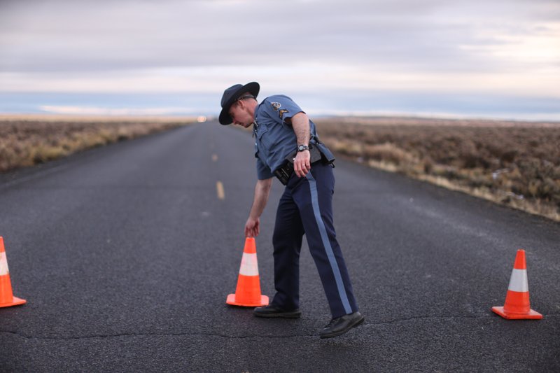 In a Jan. 28, 2016 file photo, an officer with the Oregon State Police moves a cone to establish a roadblock along one of the routes to the Malheur National Wildlife Refuge in Harney County, Ore. The FBI said Wednesday, Feb. 10, 2016, that it has moved to contain the last few occupiers of an Oregon wildlife refuge who were part of a protest that began more than a month ago over federal land policy. 