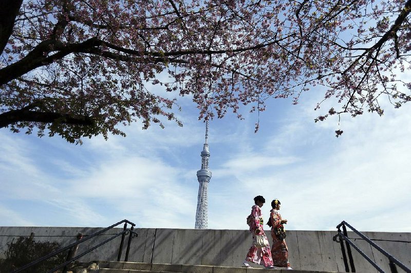 Two women in traditional Japanese clothing stroll to see cherry blossoms at Sumida Park near the Tokyo Skytree skyscraper in the background in Tokyo in 2014.
