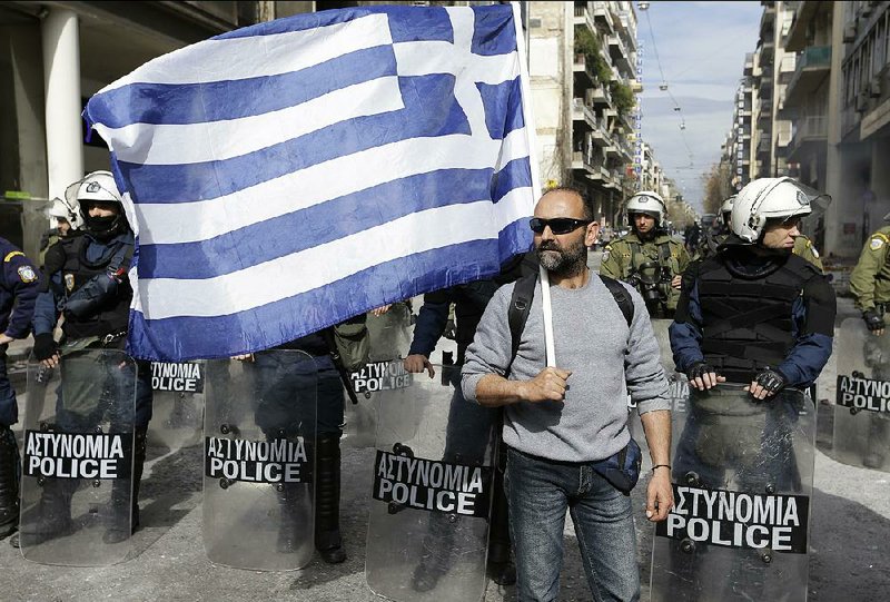 A protesting farmer holding a Greek flag stands along a line of riot police Friday in Athens.