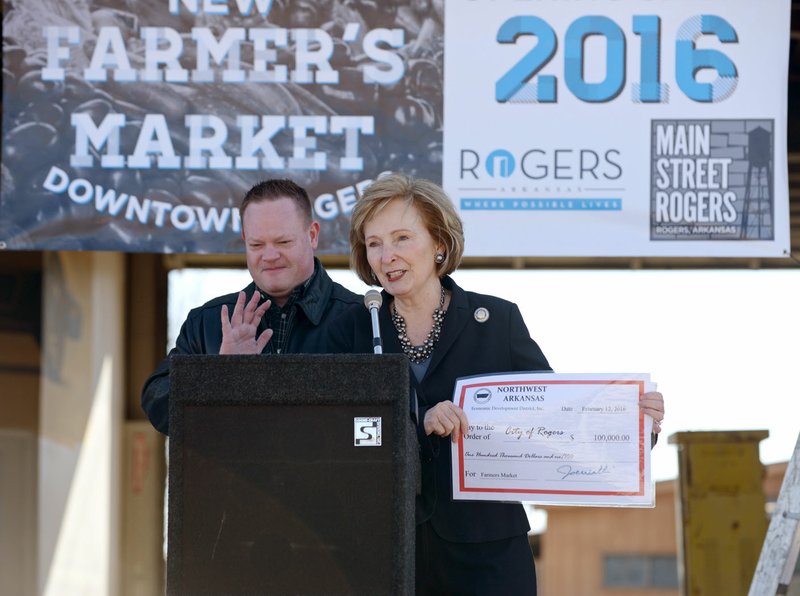 State Sen. Cecile Bledsoe, R-Rogers, presents a ceremonial check to Mayor Greg Hines on Friday during a ceremony at the site of the new Rogers Farmer's Market. Bledsoe secured $100,000 from the General Improvement Fund to help Rogers complete the project to renovate a former auto repair shop into a new indoor home for the market.