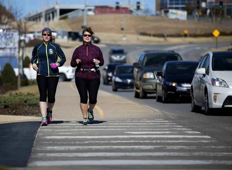 Jean Henderson (left) and Amelia Dziwanowski, both of Bentonville, jog south Wednesday along the Razorback Greenway Trail next to Village on the Creeks in Rogers.