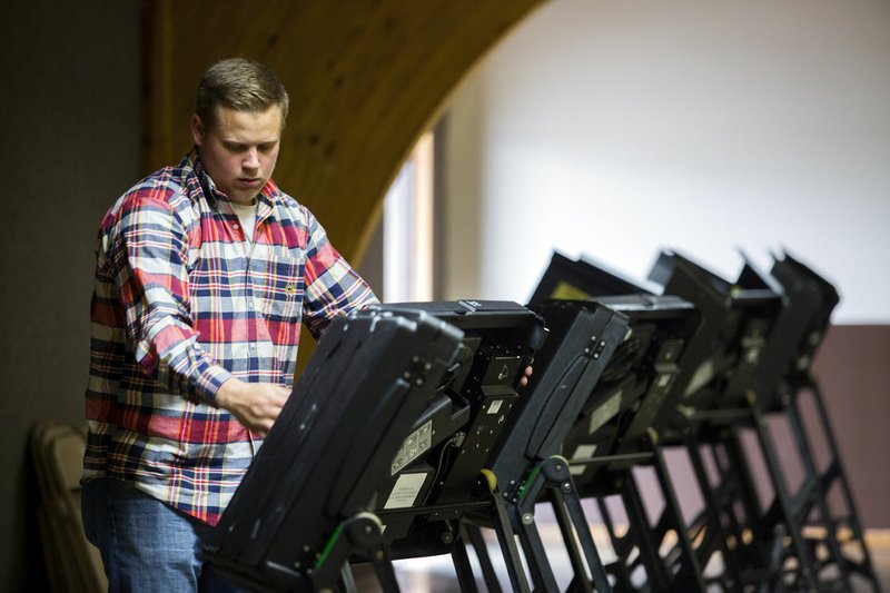 Hunter Galyon, Washington County Election Commission delivery assistant, sets up voting machines on Monday at Parsons Stadium in Springdale. Early voting begins today.