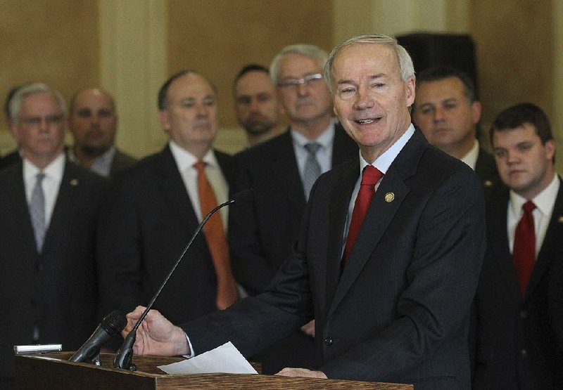 Gov. Asa Hutchinson, standing with more than 20 legislators, said Tuesday that he wanted to “debunk” arguments that supporting the state’s expanded Medicaid program means supporting the federal health care law. 