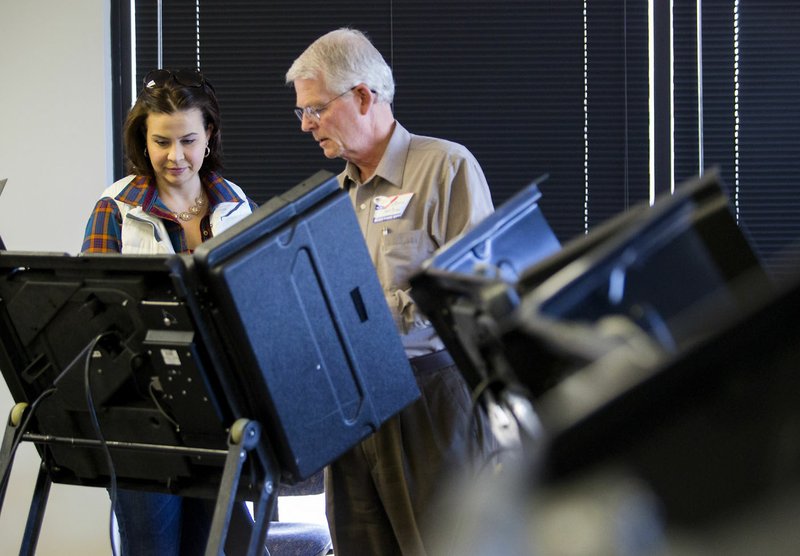John McDaniel, election worker, helps set up the voting machine Friday for Kim Minor of Bentonville at the Rogers-Lowell Area Chamber of Commerce in Lowell.