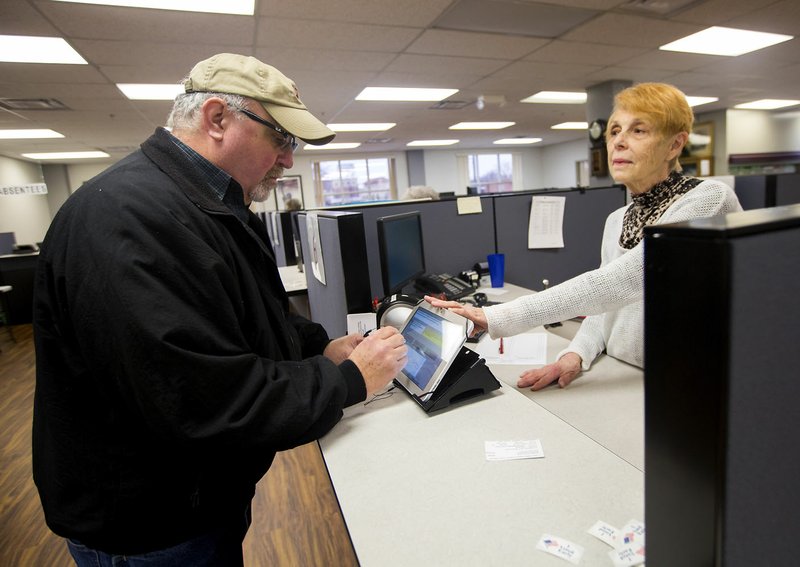 Gail Noble (right), poll worker, helps Doug Adams of Bentonville as he signs in to vote Wednesday at the Benton County Clerk’s office in Bentonville. With th addition of electronic poll books, voters can now vote in any precinct.