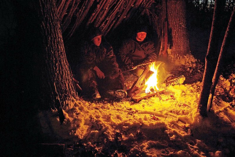 Zach Sutton, left, and Shaun Kizer warm themselves by a fire under the cover of a bivouac shelter that can keep you warm and dry if you must spend an unexpected night outdoors.