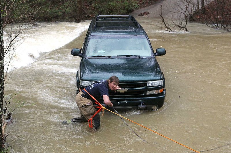 Morning Star Fire Department firefighter Joey Thompson hooks a tow line to a Chevrolet Suburban that stalled while crossing a rising Mill Creek on Pate Lane on Wednesday in Hot Springs.