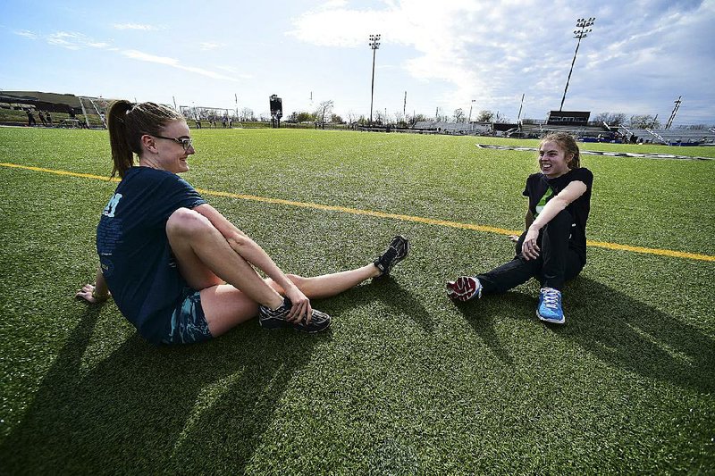 Bentonville High School junior Katie Andrews (left) stretches and visits Wednesday with Emmy Schaller, a special-needs student, at the school’s track. Andrews, who swims and runs for Bentonville High School, has been running with Schaller and helping her train for about a year.