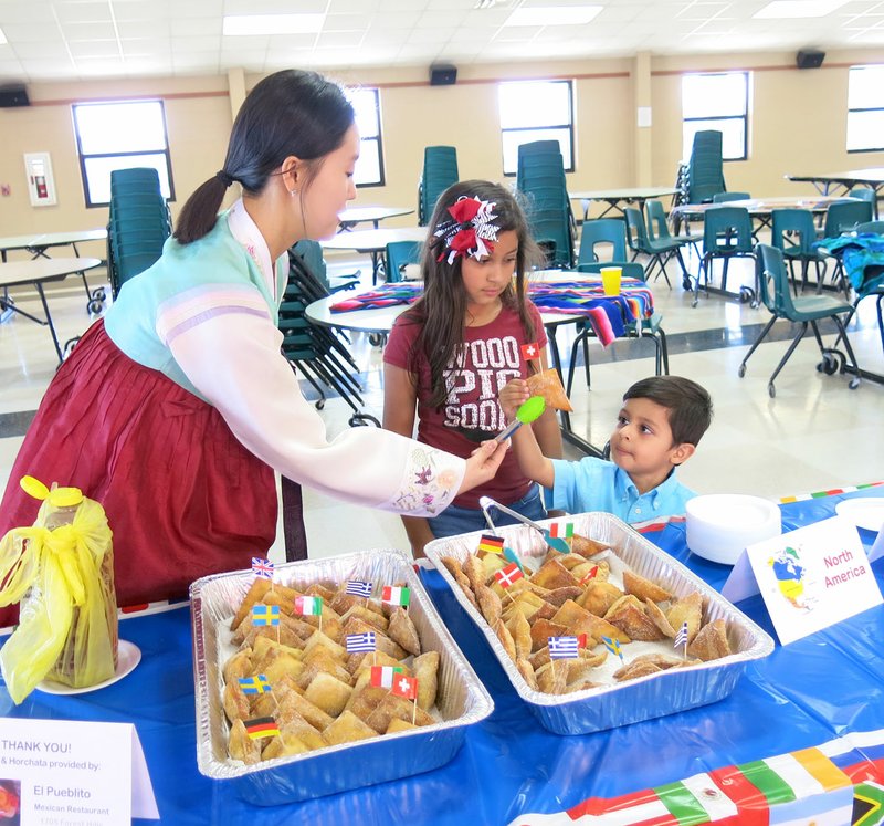 Photo by Susan Holland SangHyun (Joy) Kim, ESOL specialist at Glenn Duffy Elementary School and Gravette Upper Elementary, handed young Damian Olivarez a sopapilla to try at last Thursday&#8217;s multicultural celebration while his big sister Jasmine looked on. The Olivarez children, from Bella Vista, are students in the elementary ESOL (English for Speakers of Other Languages) program. Ms. Kim cooked the sopapillas in the special ed classroom earlier in the day.